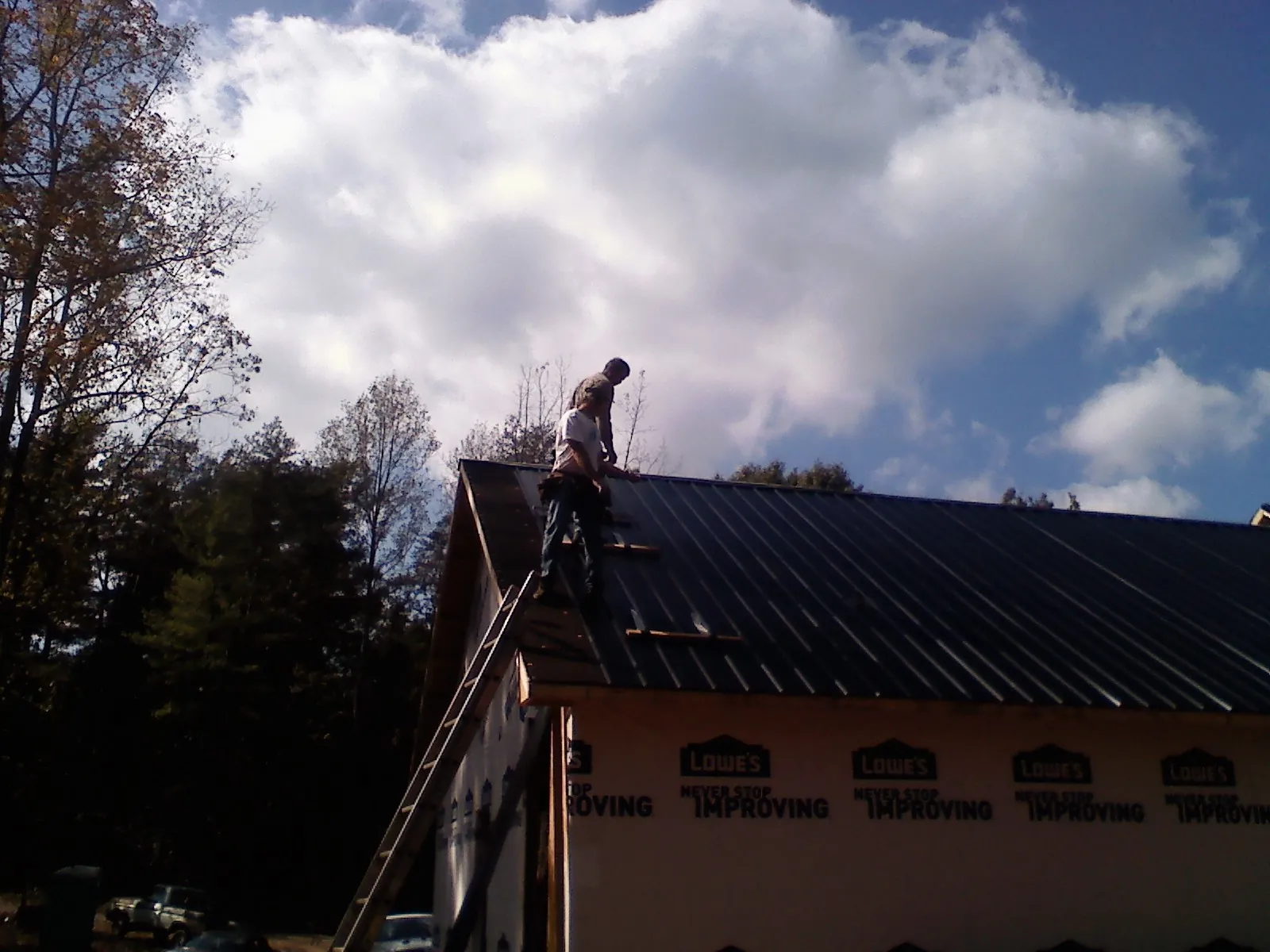 Roofer fastening dark metal panels high against a cloudy sky, from a Roof Inspection job in Umatilla