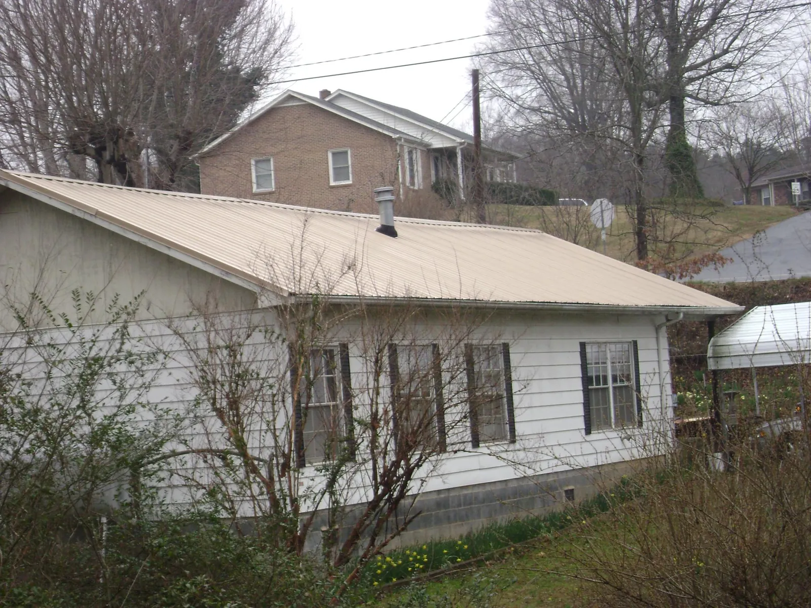 Tan metal roof on a white sided house set into a hillside — Commercial Roofing by Roofing Brothers in Umatilla